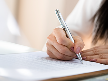Closeup of a woman holding a pen signing a paper document