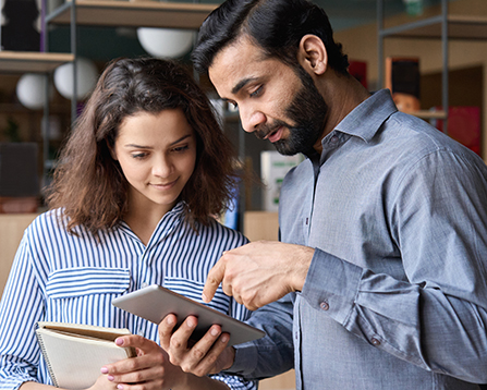Diverse friendly coworkers colleagues indian male manager and latin female employee talking in office space using tablet device. Effective management, teaching and mentoring new employee concept.