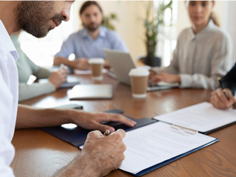 Man writing on a piece of paper at a table with colleagues during a meeting