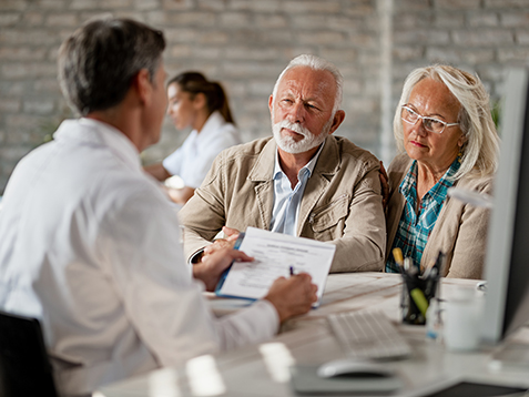 Senior couple consulting with healthcare worker about their insurance policy while having a meeting at clinic.