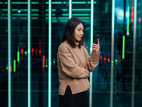 Young woman using mobile phone against futuristic holographic background. New ways of investing - using mobile app to buy stock and cryptocurrency.