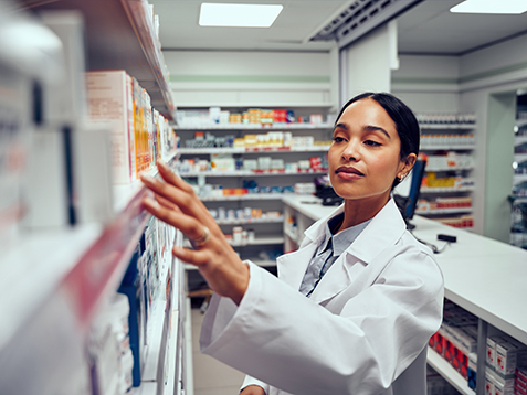 Young woman working in pharmacy looking for medicine standing behind counter