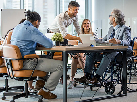 Group of business people in a meeting with colleague in a wheelchair for inclusion. Young businessman greeting handicapped business partner and team. Coworker on wheelchair