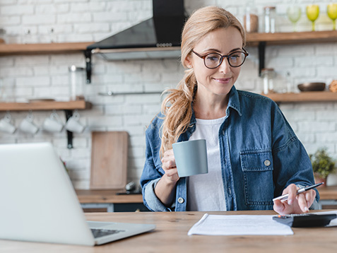 Paying bills, funds calculation on laptop at home. Mature woman counting money at home kitchen, mortgage, loan, having debt. Internet banking concept