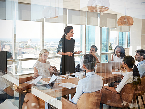 Businesswoman Leads Meeting Around Table Shot Through Door
