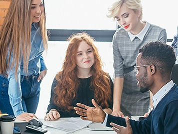 2 female employees standing around table talking to two other female and male coworkers
