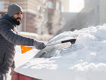 A young man cleans his car after a snowfall on a sunny, frosty day.