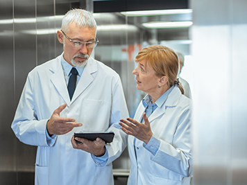 In the Hospital Two Doctors Standing in Elevator and have Discussion while Using Tablet Computer. New Modern Fully Functional Medical Facility.