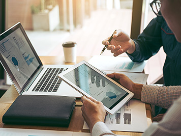 Business partnership coworkers using a tablet to chart company financial statements report and profits work progress and planning in office room.