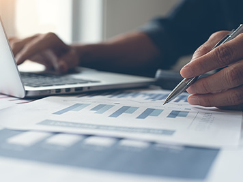 Buisness analysis. Businessman with pen in hand working on laptop computer  reviewing business marketing report on desk in office, copy space, close up. drak tone