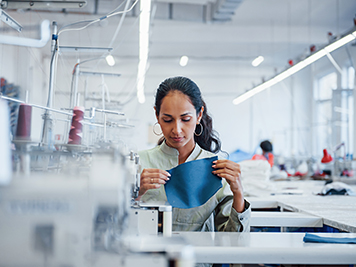 Dressmaker woman sews clothes on sewing machine in factory.