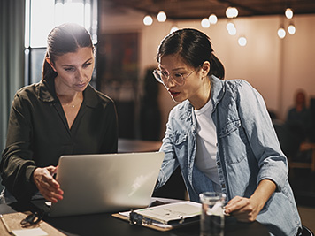 Two diverse young businesswomen working on a laptop while meeting together at a table in an office