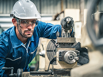 Factory worker with a hard hat and goggles using a machine