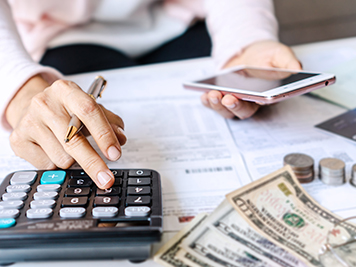 Young Asian woman holding smart phone while using calculator for business financial accounting calculate money bank loan rent payments manage expenses finances taxes doing paperwork concept, close up.