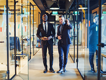 Successful businessmen in formal wear discussing trade project while walking in financial company, diverse entrepreneurs in stylish suits have office excursion for looking around tenement workspace