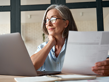 elder woman smiling while looking at computer and holding a piece of paper