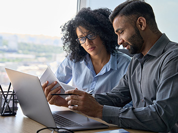 Man and woman reviewing paperwork and looking at a computer while sitting down