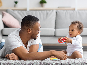 father playing with baby toys with his baby on the ground