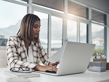 Employee using a laptop while reading paperwork.