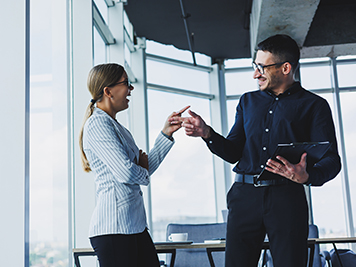 Positive businesswoman standing with Caucasian male colleague talking to businessman in office. Business relations between colleagues with smiles in a warm atmosphere