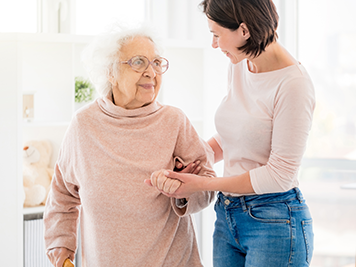 Nice woman supporting pensioner by hand standing in light room