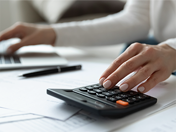 A person who has one hand working on a laptop and one hand working on a calculator