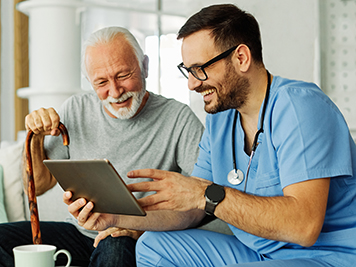 Doctor or nurse caregiver showing a tablet screen to <a href=
