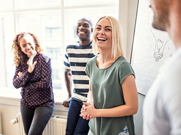 Young businesswoman laughing with a group colleagues while talking together in an office after a boardroom presentation