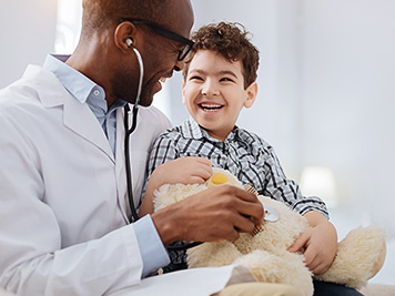 Immediate treatment. Enthusiastic vigorous male doctor sitting with boy while listening to plush bear and talking