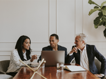 three colleagues having a meeting at a table looking at a laptop