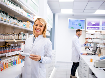 Portrait of beautiful female pharmacist standing in pharmacy store by the shelf with medicines.