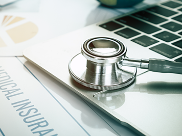 Stethoscope on computer with international medical insurance, healthcare claim forms in Doctor consulting room, report medicals fees in modern hospital on Laptop desk. Healthcare business global idea.