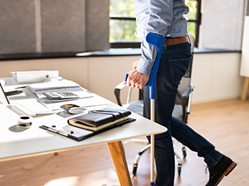 Worker With Crutches At Workplace Or Office. Rehabilitation Benefits