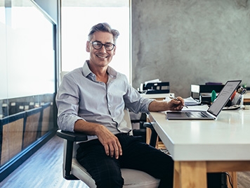 Positive mature businessman sitting at office desk. Mid adult caucasian male executive at work.