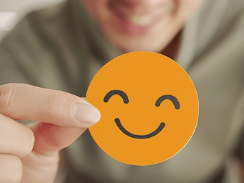 Hand holding an orange smiley face sticker