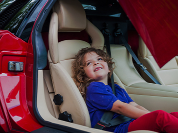 A young girl sitting in a car seat in the back of a red car
