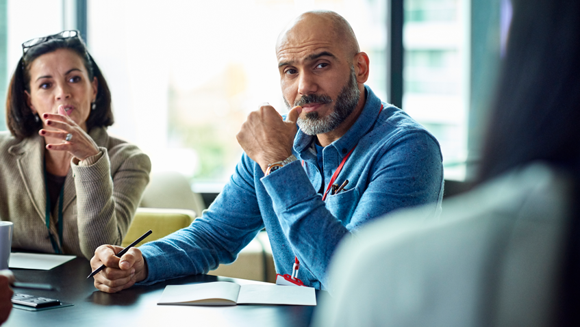 A Zebra named Ed being airlifted via helicopter in a dark mesh sack flying above the trees against blue skies.  