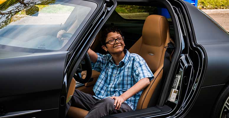 A young boy sitting inside the front seat of a sports car