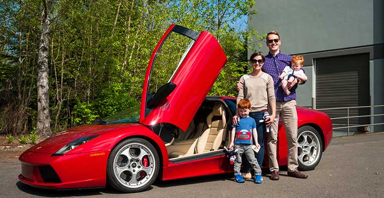 A family standing outside a red Ferrari while smiling