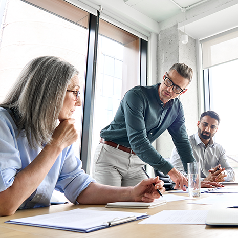 Male mature caucasian ceo businessman leader with diverse coworkers team, executive managers group at meeting. Multicultural professional businesspeople working together on research plan in boardroom.