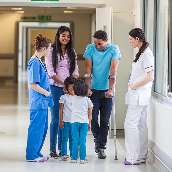 Young Asian Indian family, parents and 2 girl female children with woman doctor and nurse in modern hospital corridor